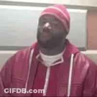 A Man Wearing A Pink Hat And A Red Jacket Is Sitting In A Chair . GIF