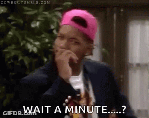 A Man Wearing A Pink Hat And A Suit Is Holding His Hand To His Chin And Says Wait A Minute . GIF