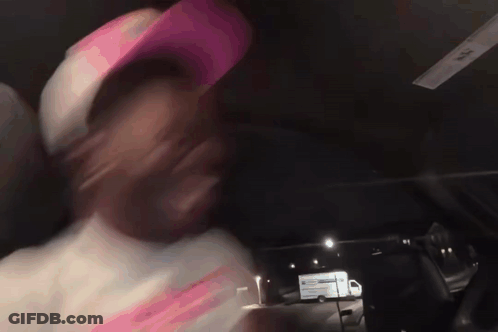 A Man Wearing A Pink Hat Is Driving A Car At Night GIF