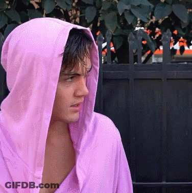 A Man Wearing A Pink Hoodie Stands In Front Of A Fence GIF