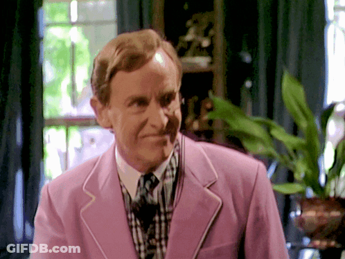 A Man Wearing A Pink Jacket And Tie Smiles GIF