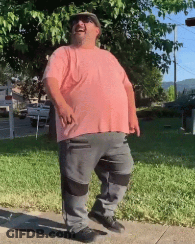 A Man Wearing A Pink Shirt And Grey Pants Is Standing On A Sidewalk GIF