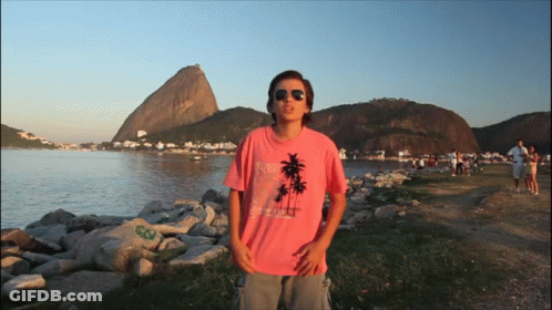 A Man Wearing A Pink Shirt With Palm Trees On It Stands In Front Of A Body Of Water GIF