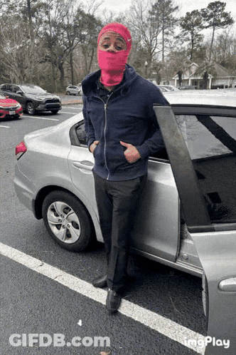 A Man Wearing A Pink Ski Mask Is Standing Next To A Car GIF