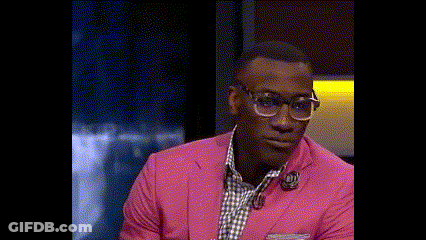 A Man Wearing A Pink Suit And Glasses Is Smiling While Sitting On A Stage . GIF