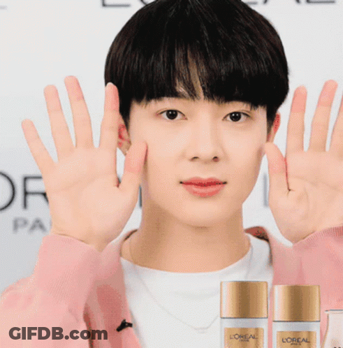 A Man Wearing A Pink Sweater Holds Up His Hands In Front Of Two Bottles Of L' Oreal Paris GIF