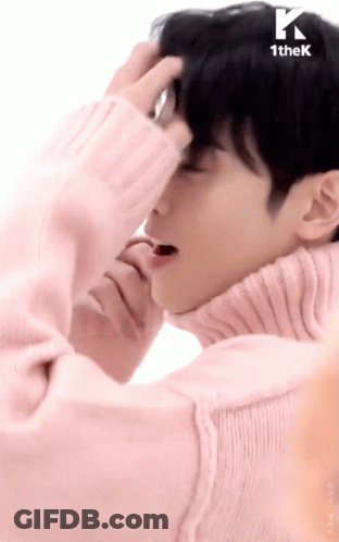 A Man Wearing A Pink Sweater Is Covering His Face With His Hand GIF