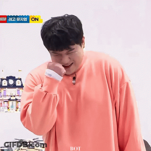 A Man Wearing A Pink Sweater Is Laughing In Front Of A Sign That Says Lego On It GIF