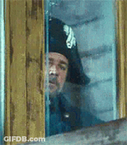 A Man Wearing A Pirate Hat Is Looking Out Of A Window GIF