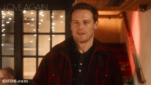 A Man Wearing A Plaid Jacket Is Standing In Front Of A Sign That Says Love Again GIF
