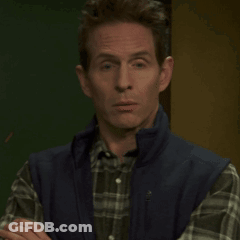 A Man Wearing A Plaid Shirt And A Blue Vest Is Looking At The Camera GIF