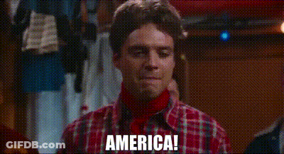 A Man Wearing A Plaid Shirt And A Red Turtleneck Is Standing In A Room And Saying `` America '' . GIF