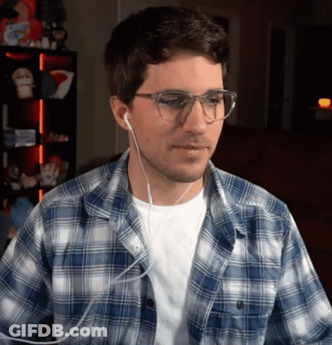 A Man Wearing A Plaid Shirt And Earbuds Looks At The Camera GIF