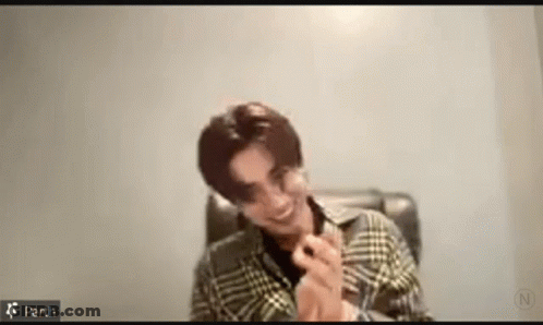 A Man Wearing A Plaid Shirt Is Sitting In A Chair And Smiling . GIF