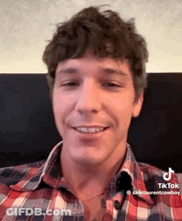 A Man Wearing A Plaid Shirt Is Smiling For The Camera . GIF