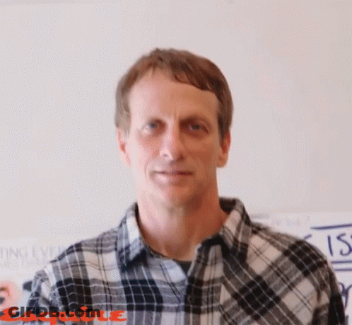 A Man Wearing A Plaid Shirt Is Standing In Front Of A Wall That Says Esquire On It GIF