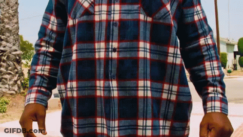 A Man Wearing A Plaid Shirt Is Standing On A Sidewalk GIF