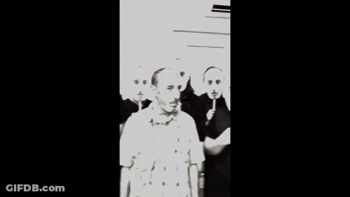 A Man Wearing A Plaid Shirt Is Surrounded By Other Men With Red Faces On Sticks GIF