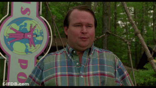 A Man Wearing A Plaid Shirt Stands In Front Of A Sign That Says Us Doo GIF