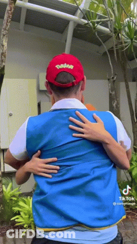 A Man Wearing A Pokemon Hat Is Hugging Another Man Wearing A Blue Vest GIF