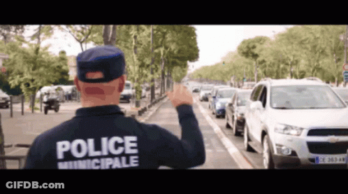 A Man Wearing A Police Municipale Jacket Stands In Front Of A Busy Street GIF