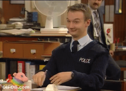 A Man Wearing A Police Sweater Sits At A Desk GIF
