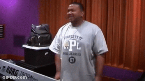 A Man Wearing A Property Of Pl Shirt Stands In Front Of A Korg Triton Keyboard GIF