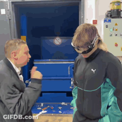 A Man Wearing A Puma Jacket Talks To A Man Wearing Goggles GIF