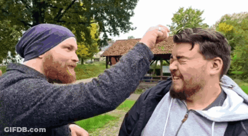 A Man Wearing A Purple Beanie Is Punching Another Man 'S Head GIF