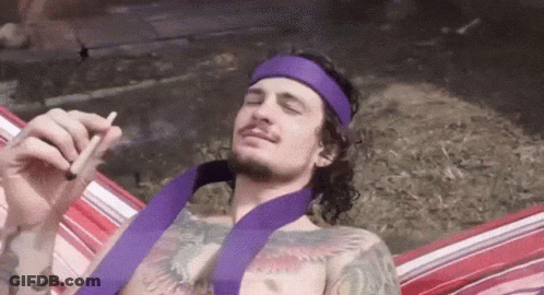 A Man Wearing A Purple Headband Is Smoking A Cigarette While Laying In A Hammock GIF