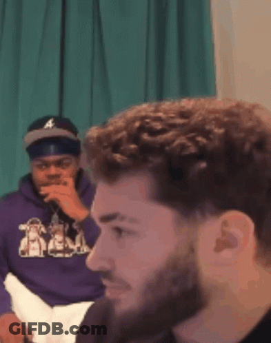 A Man Wearing A Purple Hoodie Is Sitting Next To Another Man GIF