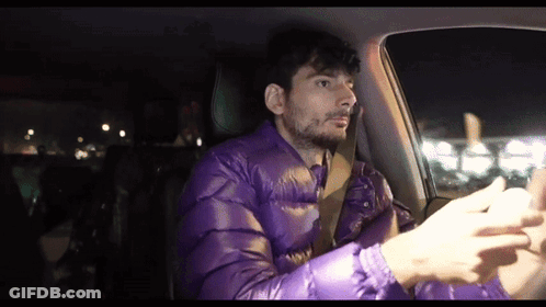 A Man Wearing A Purple Jacket Is Driving A Car GIF