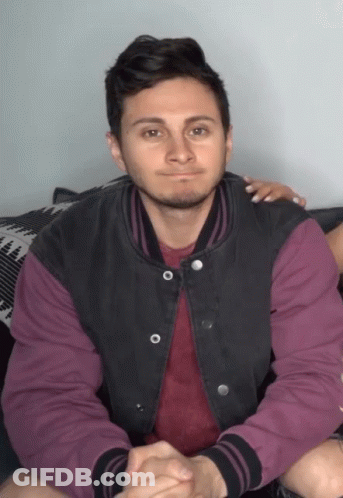 A Man Wearing A Purple Shirt And A Black Jacket Is Sitting On A Couch GIF