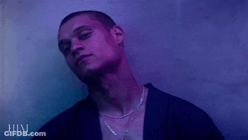 A Man Wearing A Purple Shirt And A Necklace With The Word Him Below Him GIF