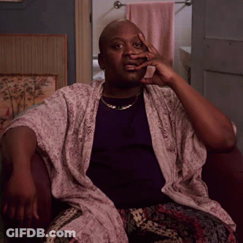 A Man Wearing A Purple Shirt And A White Robe Sits In A Chair With His Hand On His Face GIF