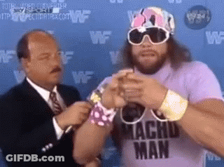 A Man Wearing A Purple Shirt That Says Macho Man Is Standing Next To A Man In A Suit And Tie . GIF