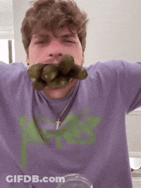 A Man Wearing A Purple Shirt With A Green Letter K On It Is Eating Pickles GIF