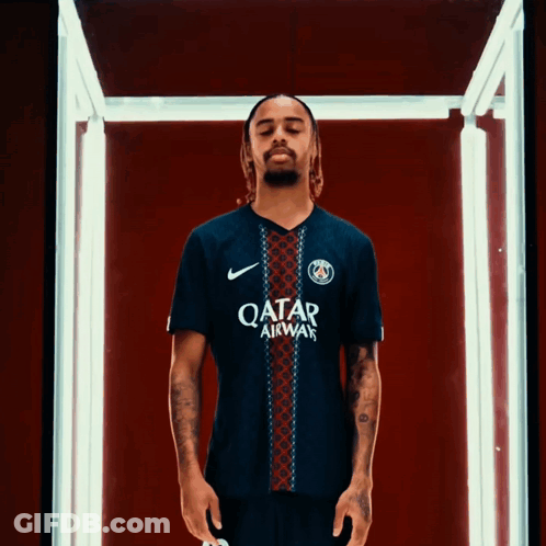 A Man Wearing A Qatar Airways Jersey Stands In A Dark Room GIF