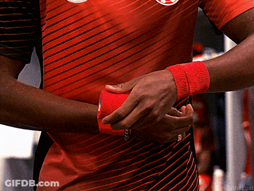 A Man Wearing A Red And Black Striped Shirt Is Wrapping His Wrist With Red Tape GIF