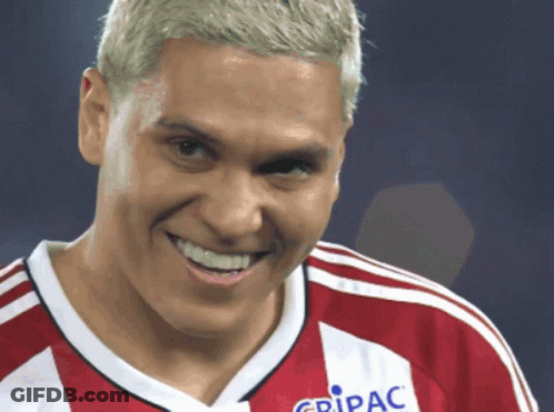 A Man Wearing A Red And White Jersey That Says Gripac Smiles GIF