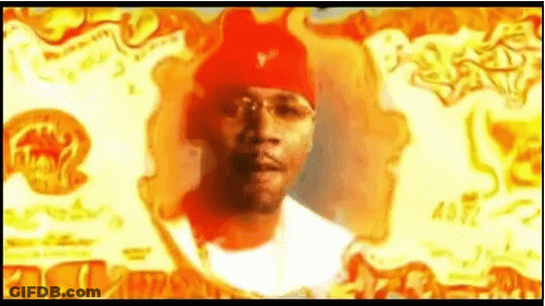 A Man Wearing A Red Beanie And Glasses Is Standing In Front Of A Fire . GIF