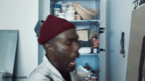 A Man Wearing A Red Beanie Is Standing In Front Of A Refrigerator . GIF