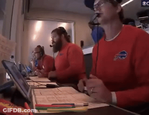 A Man Wearing A Red Buffalo Bills Sweater Is Sitting At A Desk GIF
