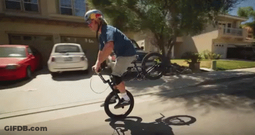 A Man Wearing A Red Bull Helmet Is Riding A Bike On A Residential Street GIF