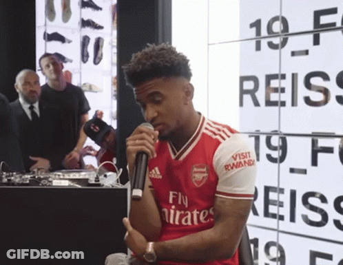A Man Wearing A Red Fly Emirates Jersey Holds A Microphone GIF