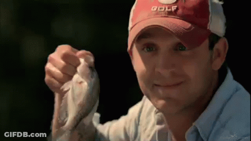 A Man Wearing A Red Golf Hat Is Holding A Small Fish In His Hand . GIF