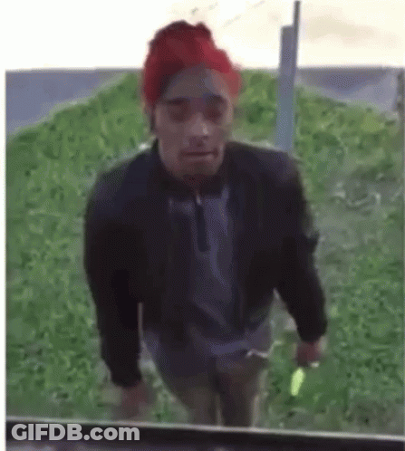 A Man Wearing A Red Hat And A Black Jacket Is Walking In The Grass . GIF