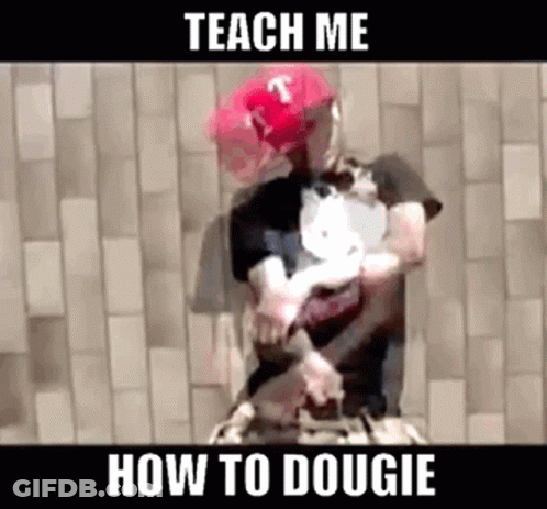 A Man Wearing A Red Hat And A Black Shirt Is Holding A Dog While Standing In Front Of A Brick Wall . GIF
