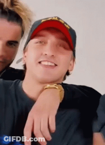 A Man Wearing A Red Hat And A Black Shirt Is Smiling . GIF