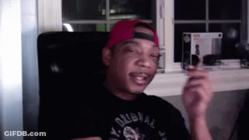 A Man Wearing A Red Hat And A Black Shirt That Says Y. Original Is Sitting In A Chair . GIF